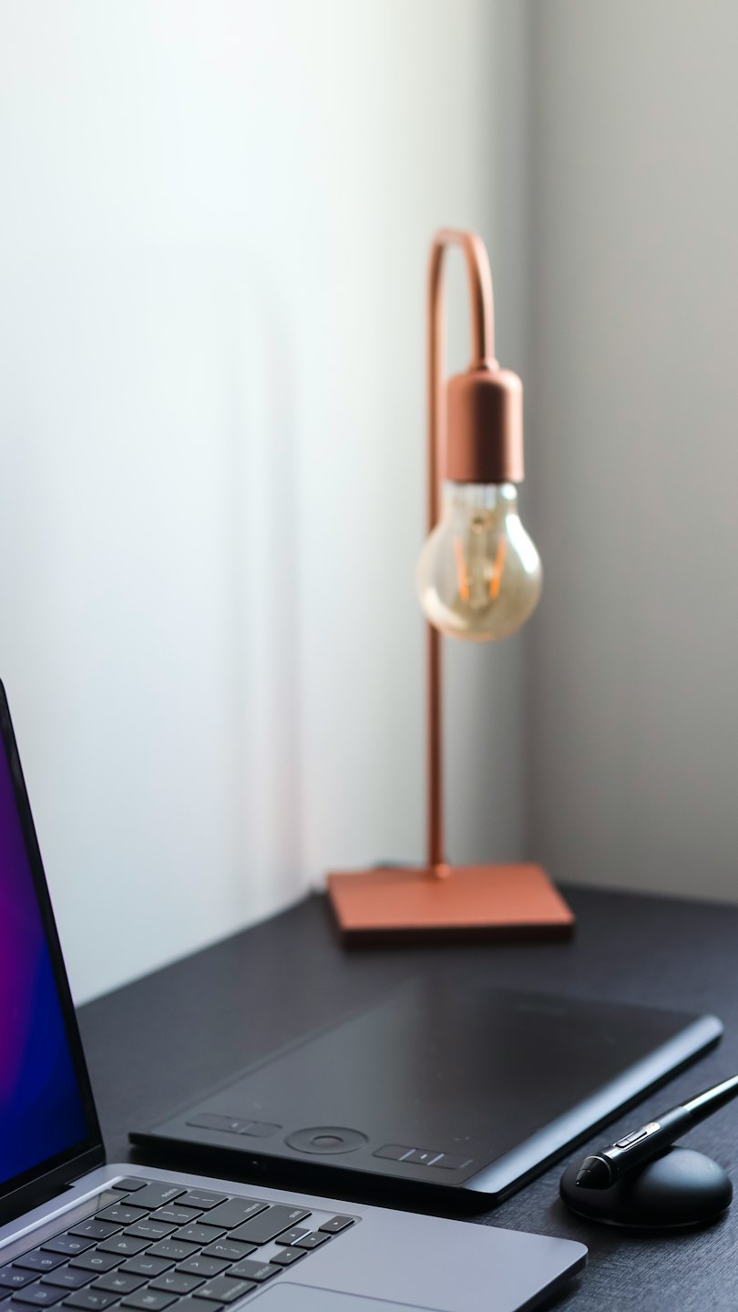 Laptop, graphics tablet, and desk lamp on a workstation.